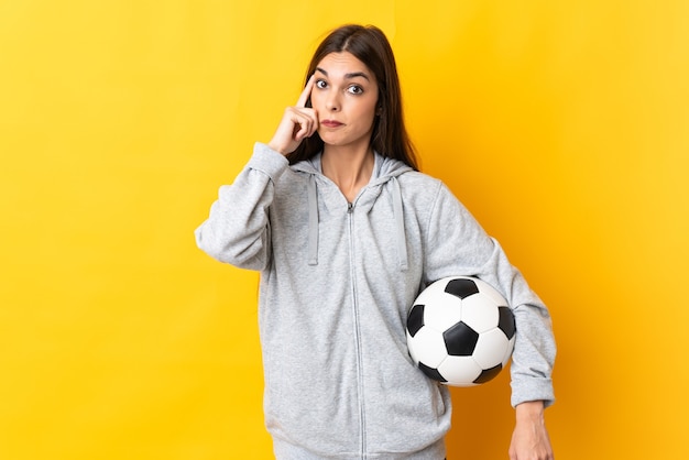 Mujer joven jugador de fútbol aislado en la pared amarilla pensando en una idea