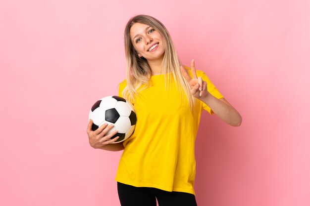 Mujer joven jugador de fútbol aislado en la pared rosa sonriendo y mostrando el signo de la victoria