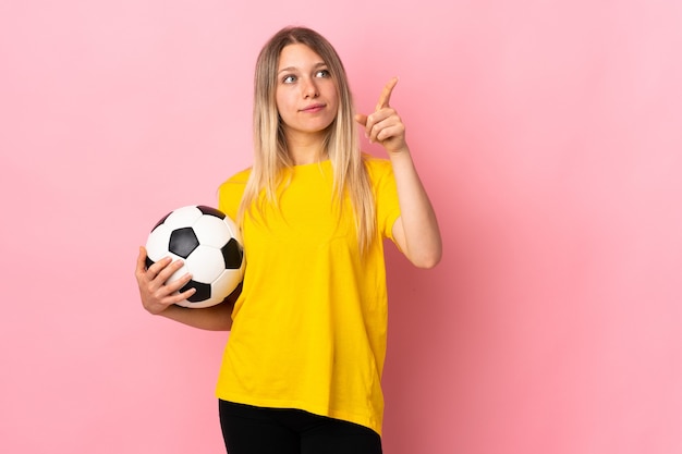 Mujer joven jugador de fútbol aislado en la pared rosa tocando en pantalla transparente