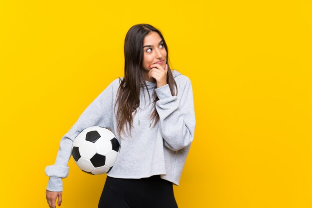 Mujer joven jugador de fútbol sobre pared amarilla aislada pensando en una idea