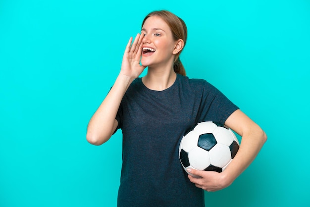 Mujer joven jugadora de fútbol aislada de fondo azul gritando con la boca abierta a un lado