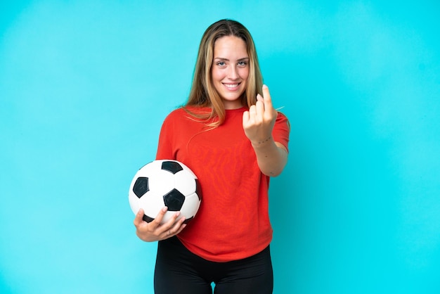 Mujer joven jugadora de fútbol aislada de fondo azul haciendo el gesto de venir