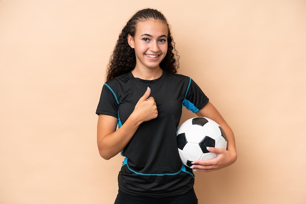 Mujer joven jugadora de fútbol aislada de fondo beige dando un gesto de pulgar hacia arriba