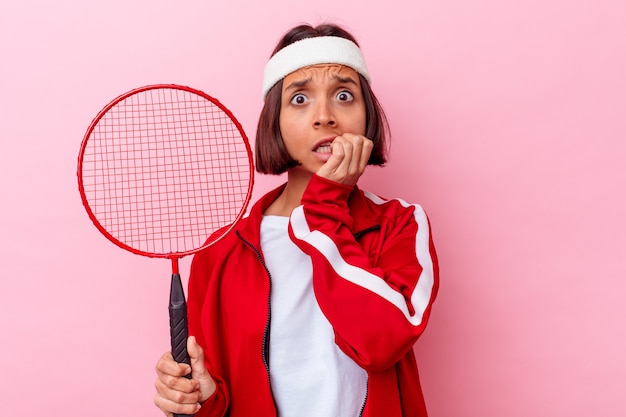 Mujer joven jugando al bádminton aislado en la pared rosa mordiéndose las uñas, nervioso y muy ansioso