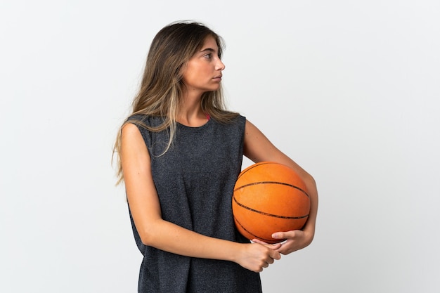 Mujer joven jugando baloncesto aislado en blanco mirando hacia el lado