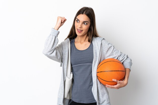 Mujer joven jugando baloncesto aislado en la pared blanca celebrando una victoria