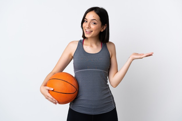 Mujer joven jugando baloncesto aislado en la pared blanca con expresión facial sorprendida