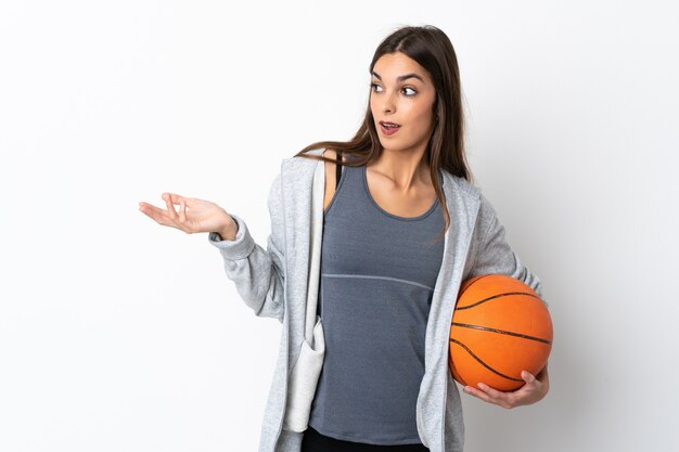 Mujer joven jugando baloncesto aislado en la pared blanca con expresión de sorpresa mientras mira de lado