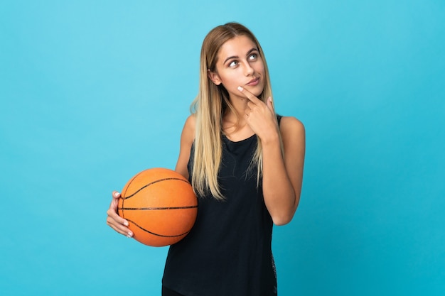 Mujer joven jugando baloncesto aislado en la pared blanca mirando hacia arriba mientras sonríe