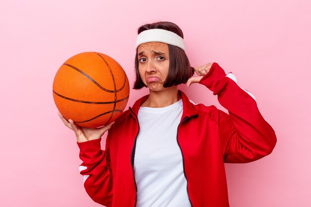 Mujer joven jugando baloncesto aislado en la pared rosa se siente orgullosa y segura de sí misma, ejemplo a seguir