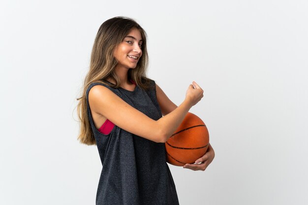 Mujer joven jugando baloncesto aislado sobre fondo blanco apuntando hacia atrás