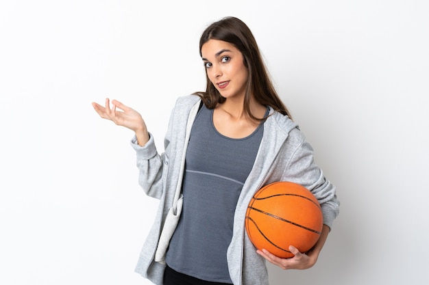 Mujer joven jugando baloncesto aislado sobre fondo blanco extendiendo las manos hacia el lado para invitar a venir