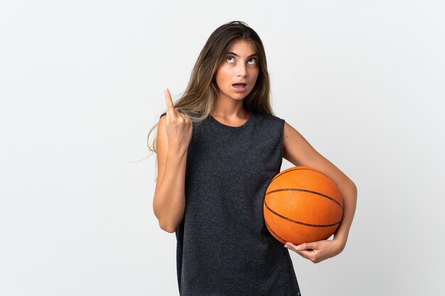 Mujer joven jugando baloncesto aislado sobre fondo blanco pensando en una idea apuntando con el dedo hacia arriba