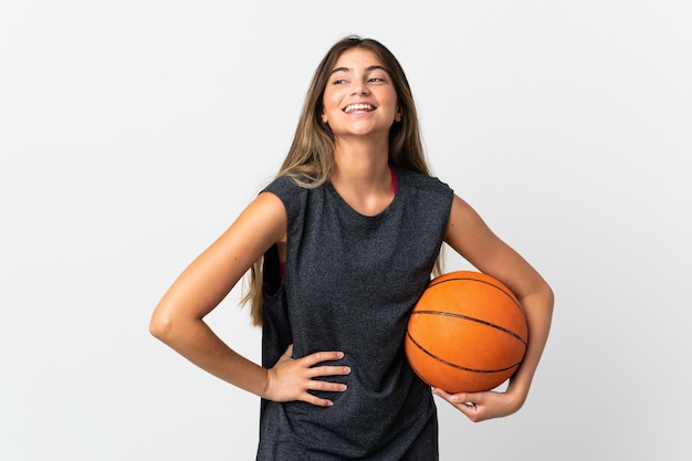 Mujer joven jugando baloncesto aislado sobre fondo blanco posando con los brazos en la cadera y sonriendo