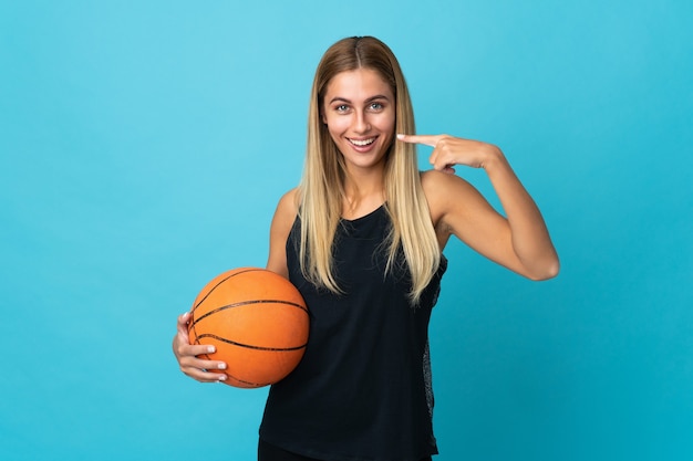 Mujer joven jugando baloncesto posando aislado contra la pared en blanco