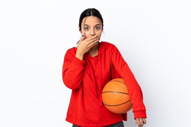 Mujer joven jugando baloncesto sobre fondo blanco aislado cubriendo la boca con la mano