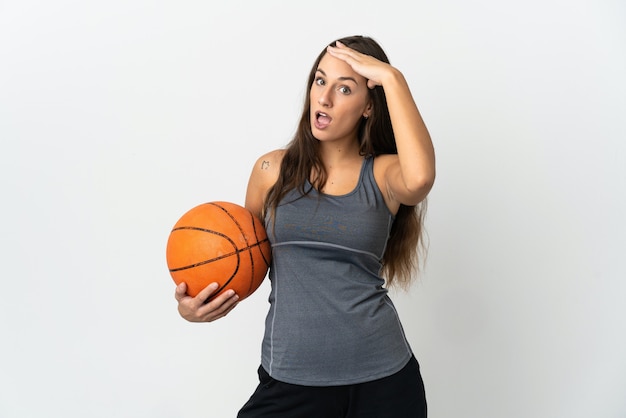 Mujer joven jugando baloncesto sobre fondo blanco aislado haciendo gesto de sorpresa mientras mira hacia el lado