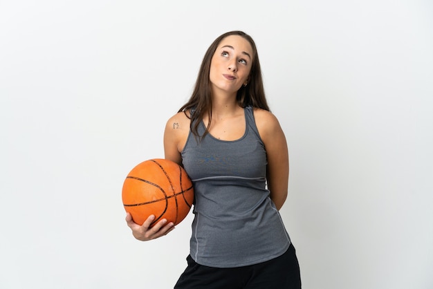 Mujer joven jugando baloncesto sobre fondo blanco aislado y mirando hacia arriba