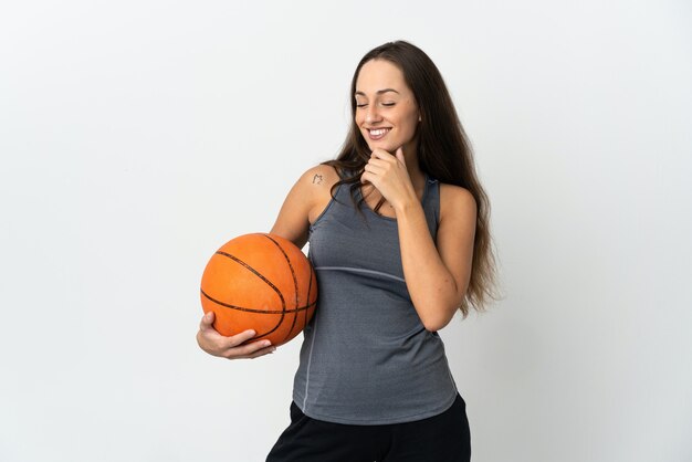 Mujer joven jugando baloncesto sobre fondo blanco aislado mirando hacia el lado y sonriendo