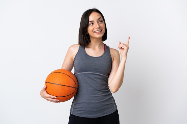Mujer joven jugando baloncesto sobre pared blanca aislada apuntando hacia una gran idea
