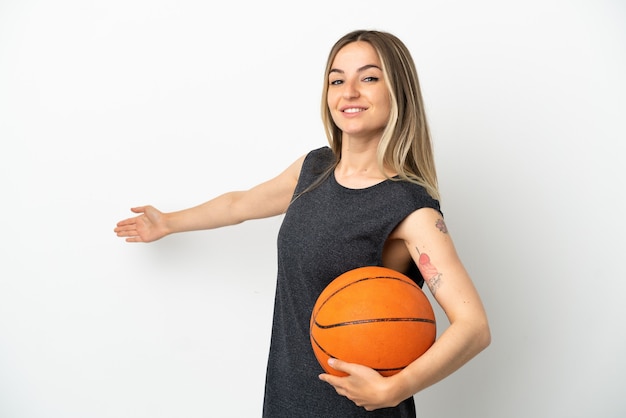 Mujer joven jugando baloncesto sobre pared blanca aislada extendiendo las manos hacia el lado para invitar a venir