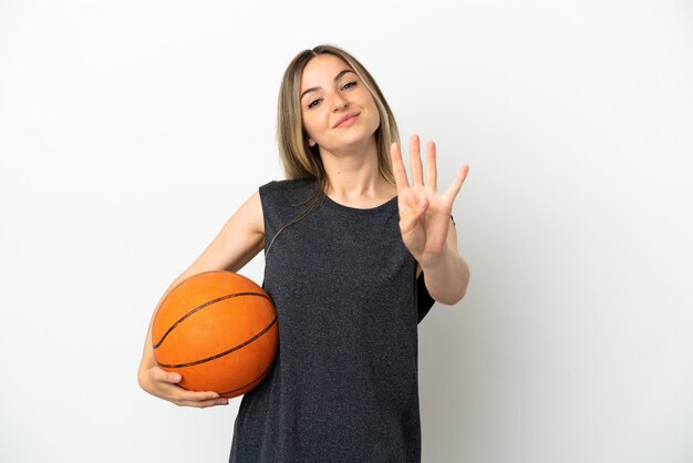 Mujer joven jugando baloncesto sobre pared blanca aislada feliz y contando cuatro con los dedos