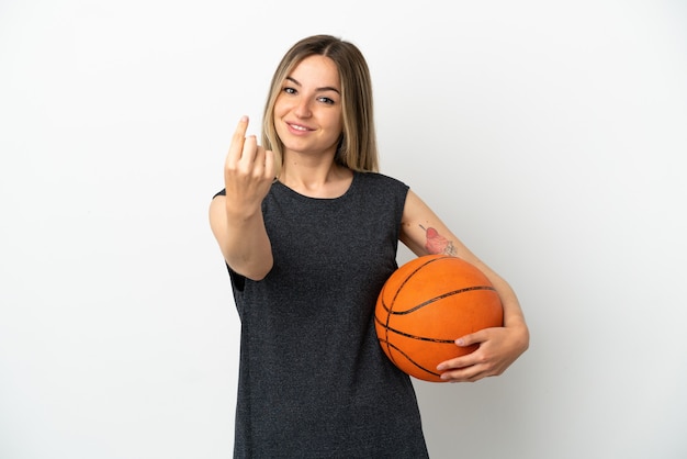 Mujer joven jugando baloncesto sobre pared blanca aislada haciendo gesto de venida