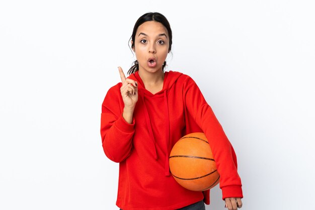 Mujer joven jugando baloncesto sobre pared blanca aislada con la intención de darse cuenta de la solución mientras levanta un dedo