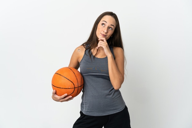 Mujer joven jugando baloncesto sobre pared blanca aislada y mirando hacia arriba