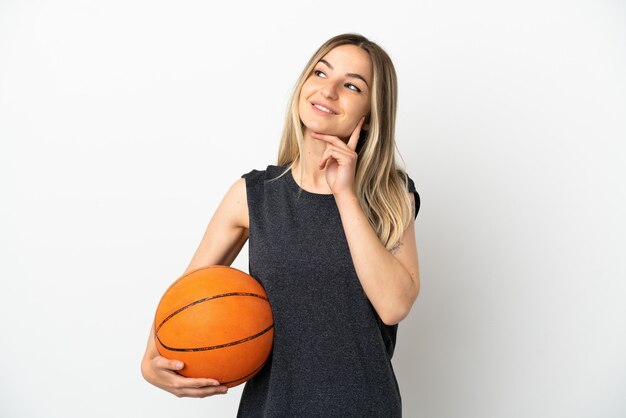 Mujer joven jugando baloncesto sobre pared blanca aislada pensando en una idea mientras mira hacia arriba