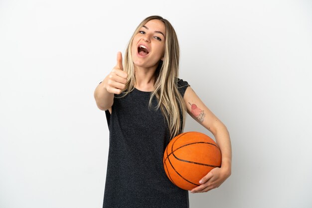 Mujer joven jugando baloncesto sobre una pared blanca aislada con los pulgares hacia arriba porque ha sucedido algo bueno