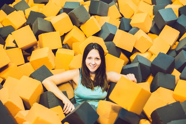 Mujer joven jugando con bloques blandos en el interior del parque infantil en el foso de gomaespuma en el centro de trampolín