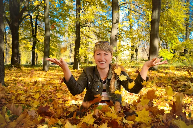 Mujer joven jugando con hojas en el brillante parque de otoño