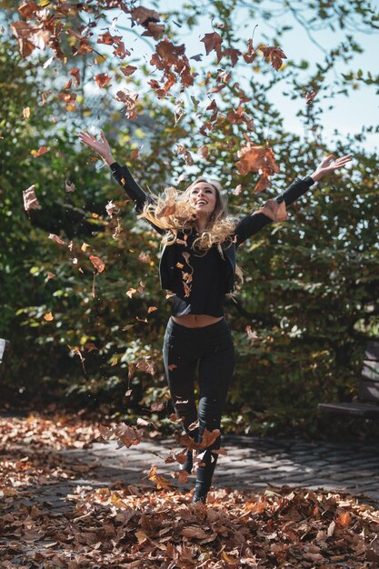 Foto mujer joven jugando con hojas en el parque durante el otoño