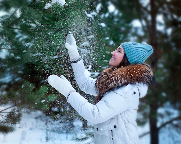 Mujer joven jugando con la nieve en el bosque de pinos de invierno Concepto de vacaciones de invierno