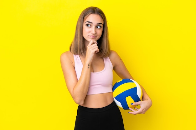 Mujer joven jugando voleibol aislado sobre fondo amarillo y mirando hacia arriba