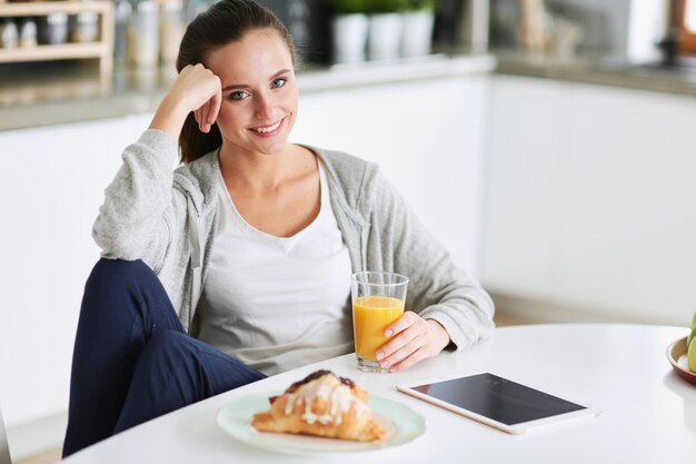 Mujer joven con jugo de naranja y tableta en la cocina.