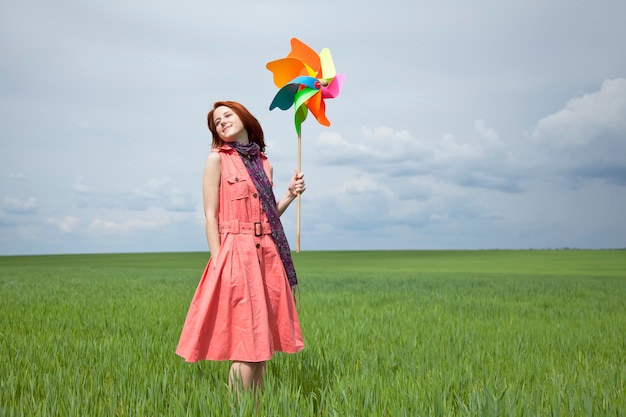Mujer joven con el juguete del molinillo de viento en campo de trigo verde