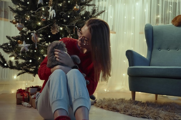 Mujer joven junto con un gato sentado cerca del árbol de Navidad Navidad con un gato mascota