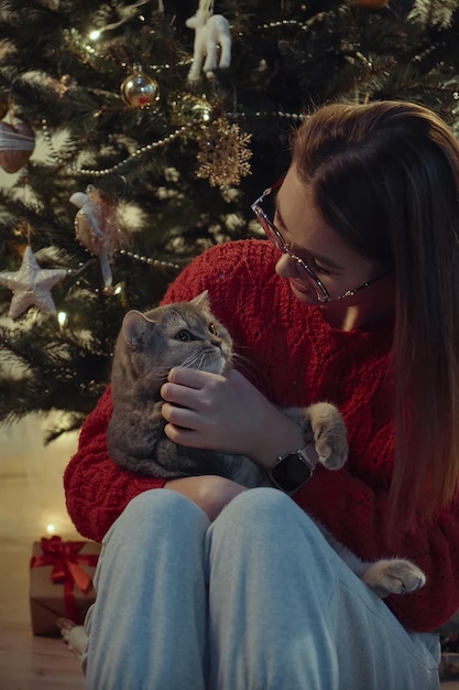 Mujer joven junto con un gato sentado cerca del árbol de Navidad Navidad con un gato mascota