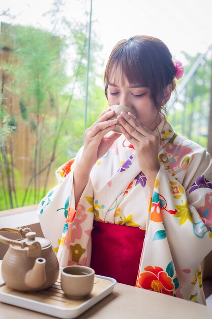 Mujer joven con kimono tradicional sentada en una casa de estilo japonés con un juego de té con fondo de jardín