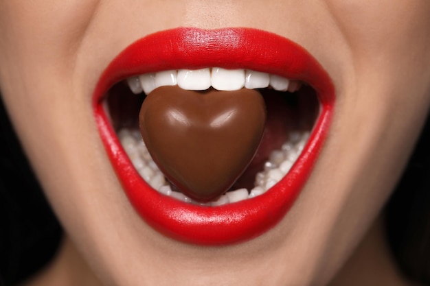 Mujer joven con labios rojos comiendo dulces de chocolate en forma de corazón closeup