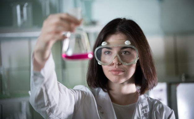 Mujer joven de laboratorio químico sosteniendo un matraz con líquido rosa en ella mujer en foco