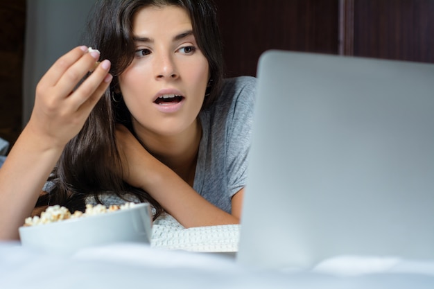 Mujer joven con laptop y comiendo palomitas de maíz