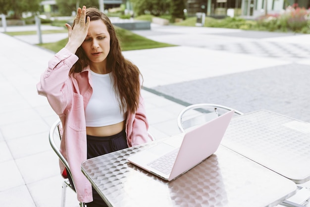 Mujer joven con laptop con gesto facepalm sintiendo arrepentimiento dolor culpándose a sí misma por error