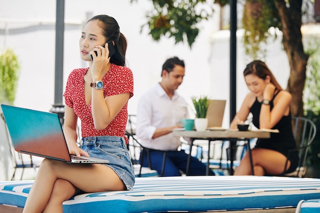 Foto mujer joven con laptop hablando por teléfono