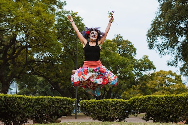 Mujer joven latina bailando y saltando en el parque vestida con un vestido largo y colorido