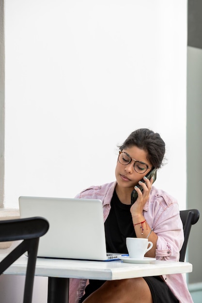 Mujer joven latina con laptop sentada en un café en la acera