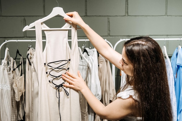 Mujer joven latina moderna que elige porcentaje de ropa de algodón orgánico en una moderna sala de exposición ecológica