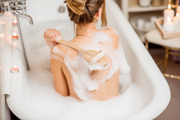 Mujer joven lavando con cepillo en el hermoso baño vintage lleno de espuma en el baño decorado con velas